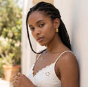 Woman with braided hair wearing a white top and gold jewelry outdoors.