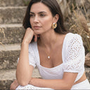 Woman in a white dress with gold jewellery sitting on steps outdoors