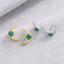 Gold and silver earrings with green gemstones on a light gray fabric background