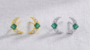 Pair of gold and silver moon-shaped earrings with green gemstones on a textured gray background