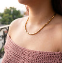 Gold chain necklace worn by a person with a blurred outdoor background