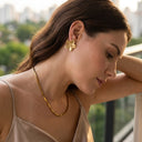 Woman wearing gold earrings and necklace with blurred outdoor background