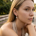 Woman with a thoughtful expression sitting outdoors, wearing a silver earring.