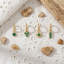 Gold earrings with green gemstones on a textured white surface with stones around.