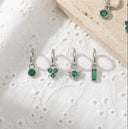 Set of silver earrings with green gemstones on a textured white surface