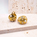Gold earrings with embedded pearls and crystals on a textured surface