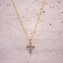 Gold cross necklace with small stones on a textured beige surface