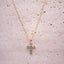 Gold cross necklace with small stones on a textured beige surface