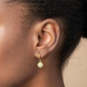 Close-up of an ear wearing Mini Gold Huggie Hoop Earrings with Sunflower Charm