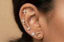 Close-up of an ear with multiple earrings including crosses, a moon, and a star.
