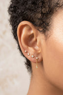 Close-up of an ear wearing gold earrings with a neutral background