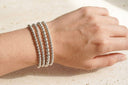 Hand wearing three silver beaded bracelets on a light background