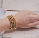 Gold beaded bracelet on a wrist with a neutral background