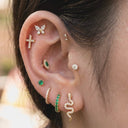Close-up of an ear with multiple diamond and emerald earrings.