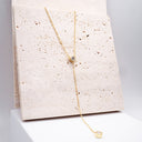 Moissanite Drop Pendant Necklace. Gold necklace with a small pendant on a textured beige card
