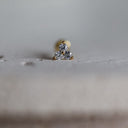 Small gold earring with a clear gemstone on a light fabric background