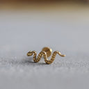 Gold snake-shaped earring on a light grey surface