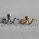 Gold and silver snake-shaped earrings on a textured surface