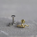 Two small snake earrings, one silver and one gold, on a grey surface.