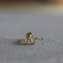 Gold snake-shaped earring on a textured surface