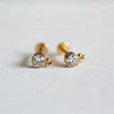 Gold earrings with clear gemstones on a light grey background