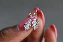 Silver leaf earrings held between fingers with a blurred background
