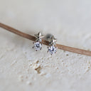 Silver star-shaped earrings with clear stones on a light beige background