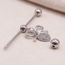 Silver earring with bow and ball charm on a textured surface
