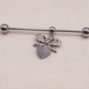 Silver Industrial Earring with a bow and heart charm on a beige background