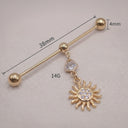 Gold Industrial piercing barbell with sun design and clear gemstone on a textured surface