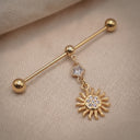 Gold industrial piercing with sun design and clear gemstone on a textured surface