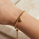 Gold bracelet with acorn charm on a wrist against a neutral background