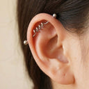 Close-up of an ear with a silver wave barbell industrial cartilage earring on a neutral background