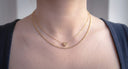 Close-up of a person wearing two gold necklaces with a heart pendant.