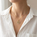 Gold necklace with a tree of life pendant worn by a person in a white shirt.