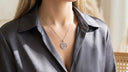 Person wearing a silver necklace with a tree pendant on a blurred background