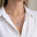 Silver necklace with a tree-of-life pendant worn by a person in a white shirt.