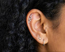 Close-up of an ear with a small silver snake earring, hair, and skin texture.