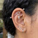 Close-up of an ear with multiple earrings including a cross pendant Industrial Piercing