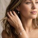 Woman wearing a silver leaf earring and bracelet against a neutral background