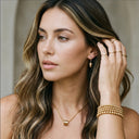 Woman wearing gold jewelry including earrings, necklace, and bracelets.