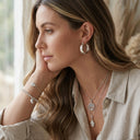 Woman wearing silver jewelry including earrings, necklace, and bracelet, sitting indoors.