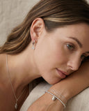Woman wearing silver earrings, necklace, and bracelet with a neutral background