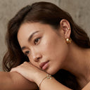 Woman wearing gold Hoop earrings and bracelet against a neutral background