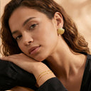 Woman wearing gold earrings and bracelets against a warm-toned background