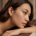 Woman wearing a gold triangle earring with a neutral background