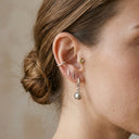 Close-up of a person's ear with multiple earrings against a neutral background