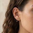 Close-up of an ear with gold earrings against a neutral background