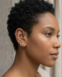 Close-up of a woman's ear with multiple earrings against a neutral background