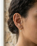 Close-up of an ear with multiple gold and diamond earrings against a blurred natural background